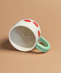 White cup with red spots and a green handle on a cardboard surface
