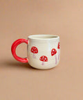 Ceramic mug with red handle and mushroom design on a beige background