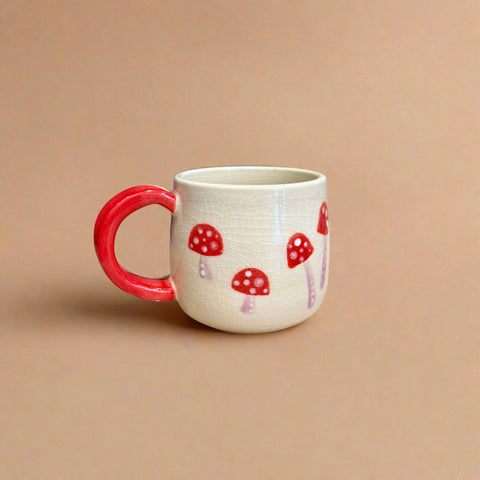 Ceramic mug with red handle and mushroom design on a beige background