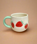 Ceramic mug with strawberry design on a cardboard surface