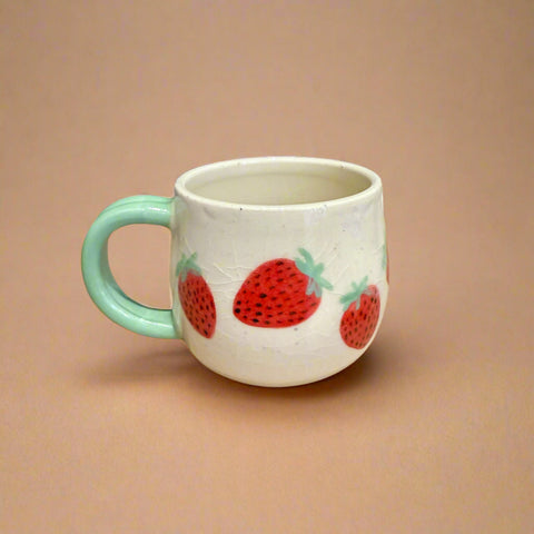 Ceramic mug with strawberry design on a cardboard surface