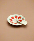 Small ceramic plate with strawberry design on a cardboard surface