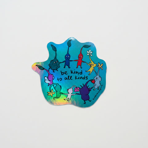 Holographic sticker with cartoon characters and 'be kind to all kinds' text on a wooden surface