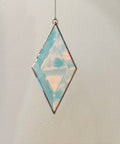 Diamond-shaped pendant with iridescent finish on a chain against a neutral background