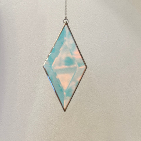 Diamond-shaped pendant with iridescent finish on a chain against a neutral background