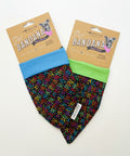 Two pet bandanas by MomeMade displayed on a light wood surface. One bandana is light blue with a multicolor alphabet print, and the other is lime green with the same multicolor alphabet print.