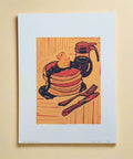 Woodcut-style illustration of pancakes with syrup, a fork, and knife on a wooden surface.