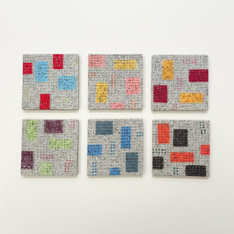 Six square ceramic coasters with abstract geometric patterns in various colors, arranged in a 2x3 grid on a light wood surface.