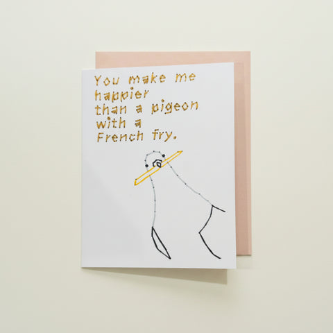 A white greeting card with a humorous quote and a simple drawing, placed on a light pink envelope over a wooden surface.