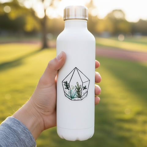A die-cut sticker featuring a hand-drawn geometric terrarium with succulents, placed on a light wood surface.