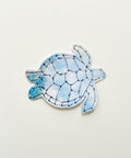 A small sea turtle-shaped sticker with a blue and white watercolor-style shell design.
