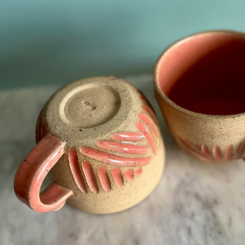 Two ceramic mugs with pink handles and decorative elements on a marble surface.