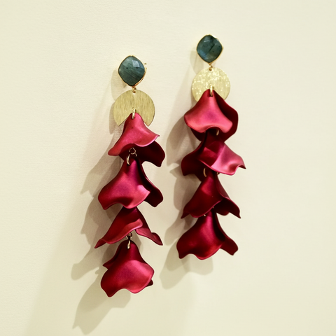 Red floral earrings with gold and black accents on a textured light gray background