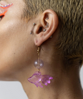 Close-up of a person wearing a purple fish earring with a plain background