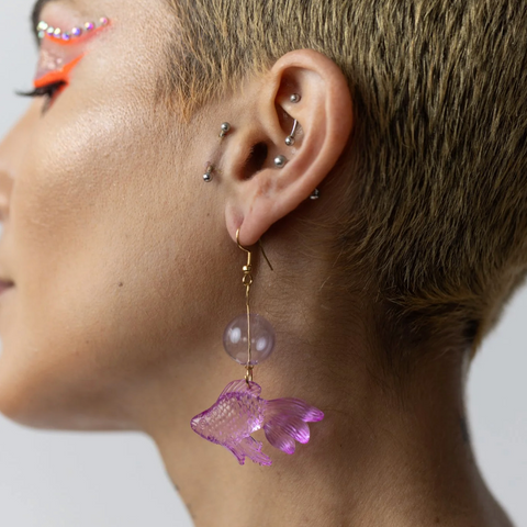 Close-up of a person wearing a purple fish earring with a plain background