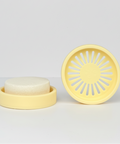A cream colored circular silicone shower steamer tray with a sunburst cutout pattern.