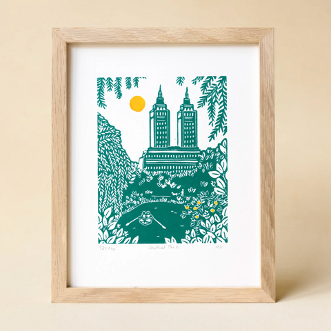 Framed artwork of a cityscape with trees and a river on a beige background