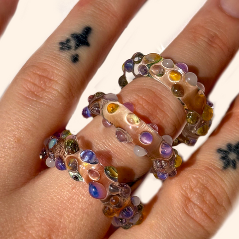 Close-up of a hand wearing a colorful beaded ring on a white background