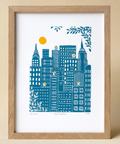 Framed artwork of a cityscape with blue buildings and a yellow sun on a beige background