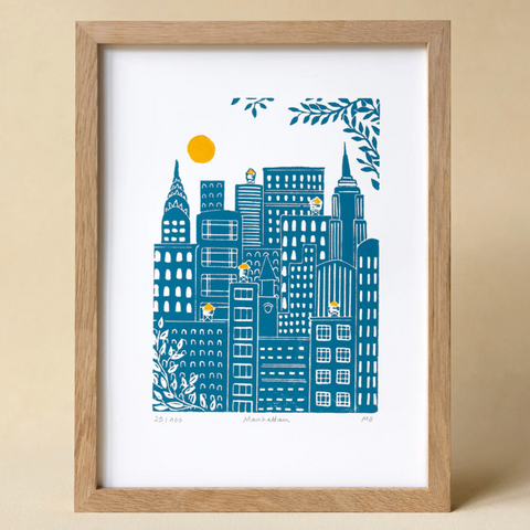 Framed artwork of a cityscape with blue buildings and a yellow sun on a beige background
