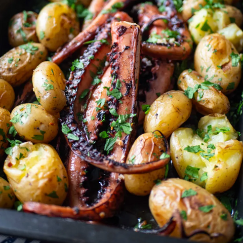 Grilled octopus with roasted potatoes and herbs in a black dish