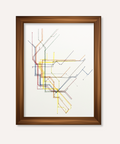 Framed abstract transit map art print with multicolored intersecting lines on a white background, enclosed in a medium brown wood frame against a light beige wall.