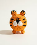 A crocheted orange tiger toy with black stripes and a white nose sits on top of a clear glass bottle against a plain white background.