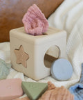 Wooden block toy with various shapes and a pink shell on a soft surface