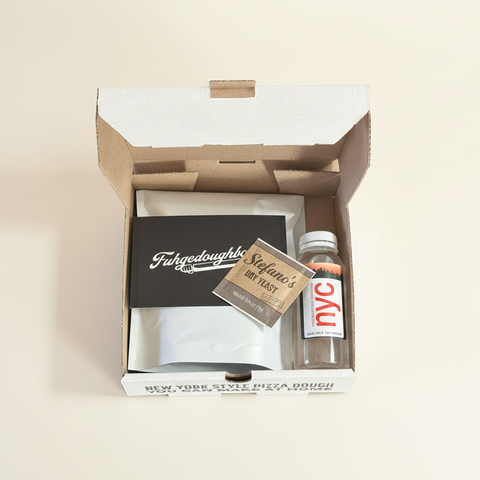 Open box containing pizza dough ingredients, a packet of yeast, and a small container of NYC tap water.